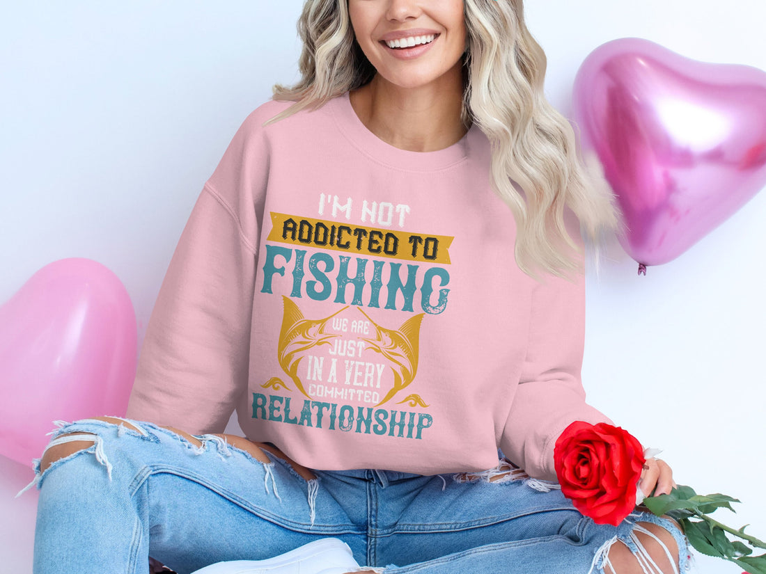 A white sweatshirt from Garment Graphics with unisex sizing displays Addicted to Fishing, Relationship and fish graphics. Its styled on a wooden surface with a mustard blazer, sunglasses, makeup brushes and palette, pink loafers, nail polish, and a pouch.