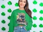 A woman smiles brightly in front of a shamrock wall, wearing Garment Graphics graphic sweatshirt with a truck design and Keep On Trucking phrase, paired comfortably with blue jeans thanks to its unisex sizing.