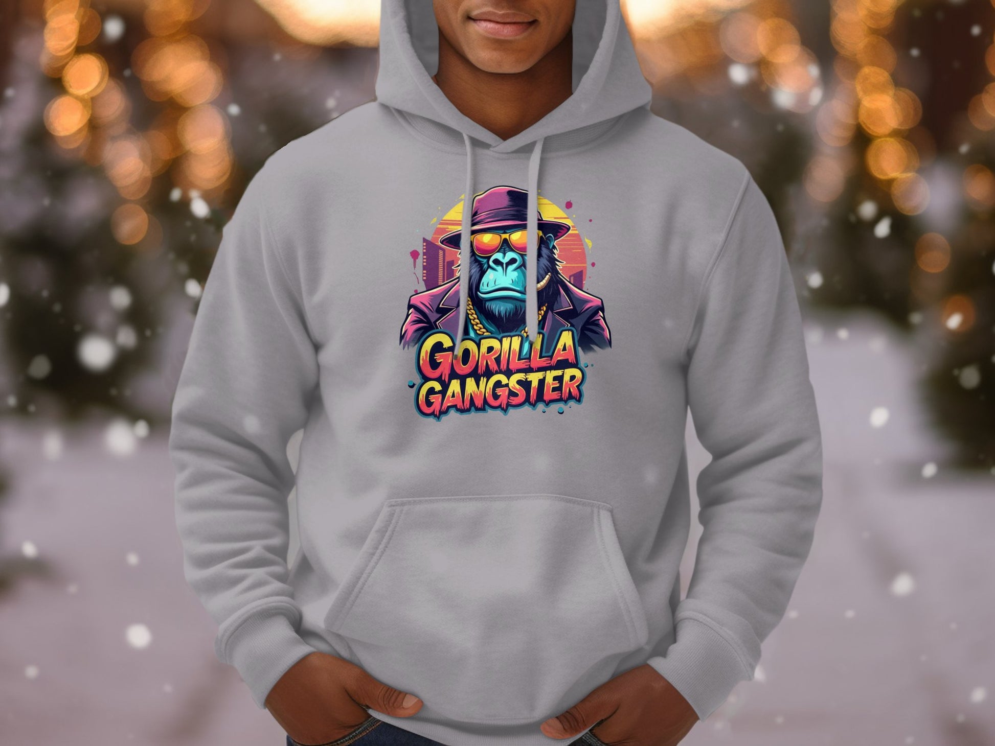 A person wears a Garment Graphics gray hoodie featuring colorful gorillas, with one in sunglasses and a hat. The Gorilla Gangster text adds flair to this streetwear piece, while blurred snowflakes in the background enhance its edgy vibe.