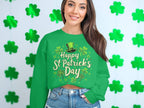 A woman with long dark hair beams in a Garment Graphics green sweatshirt featuring Happy St. Patricks Day and shamrock designs, exuding festive cheer as she stands against a wall of green shamrock cutouts.