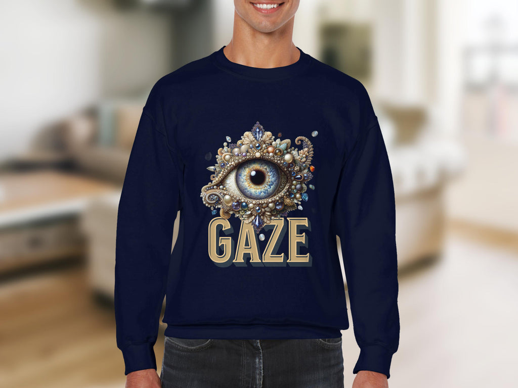 A person wearing a navy blue Garment Graphics sweatshirt with an ornate eye design above GAZE is indoors. The blurred background with neutral tones highlights the unisex appeal of this stylish garment.
