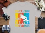 A gray t-shirt by Garment Graphics features a DJ graphic with a headphone-wearing silhouette and turntables against vibrant stripes. The phrase Dont Stop the Music stands out, making it ideal for music fans. Displayed on wood among assorted items, its perfect for lively gatherings.
