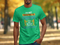 A Garment Graphics T-shirt, in green, showcases a hook design with the slogan Im not addicted to fishing, we are just in a very committed relationship. It is worn by someone on an outdoor path lined with autumn trees—a fitting scene for devoted anglers.