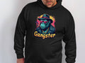 A person sports a Garment Graphics black hoodie featuring a stylish illustration of a chimpanzee in a suit and hat, wearing pink sunglasses, with Gangster written below.