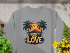 Garment Graphics gray sweatshirt showcases a One Love Sunset design with palm trees, a sunset, a plane above mountains, and is framed by green plants and yellow flowers, capturing carefree vibes.