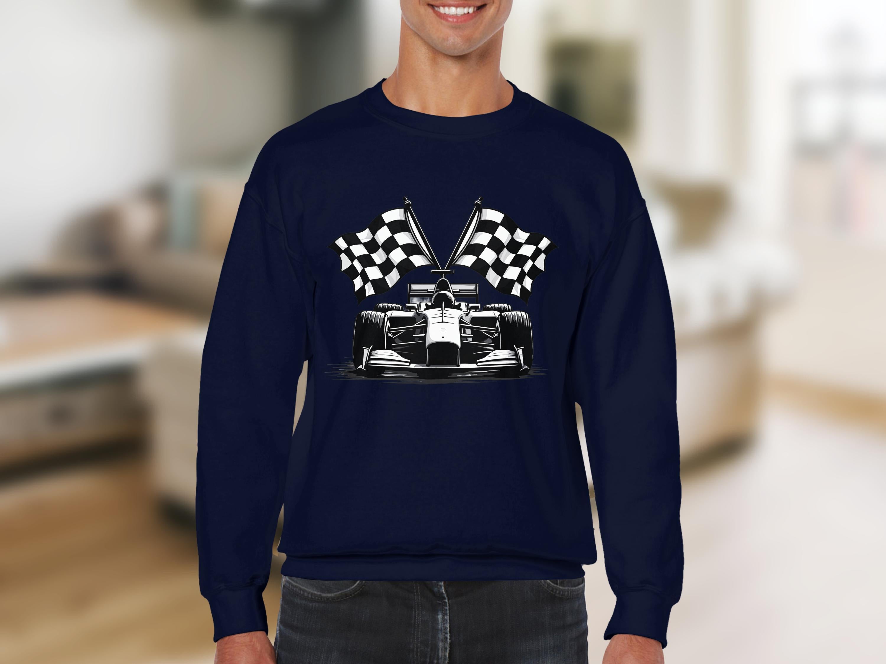 A person is wearing a Garment Graphics dark blue racing car sweatshirt, featuring a race car graphic with crossed checkered flags, against the blurred background of an interior room with a couch and shelves.