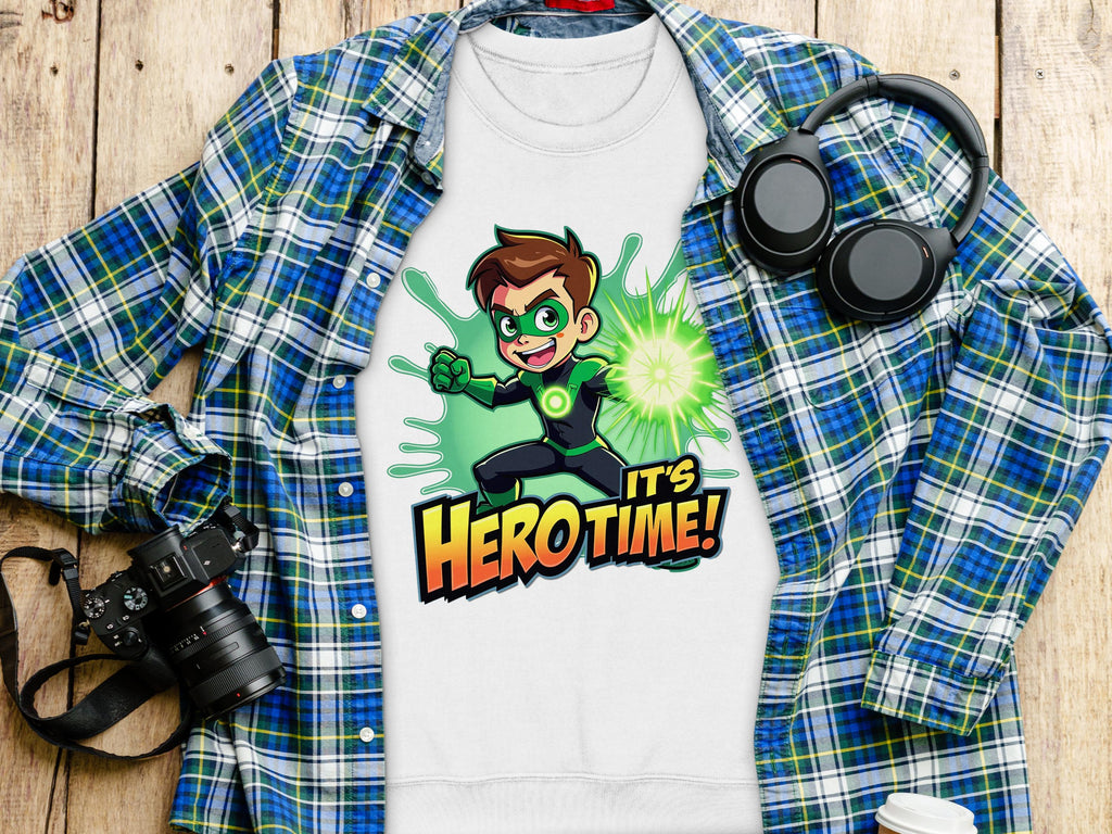 A Garment Graphics white sweatshirt with an Its Herotime superhero cartoon and vibrant green splashes is styled over a blue plaid shirt. Nearby, headphones, a camera, and a white coffee cup sit on the wooden surface—ideal for adventure-loving youth.