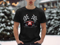 Wearing a sleek Garment Graphics black T-shirt featuring a red race car and crossed checkered flags, a motorsport enthusiast contrasts the snowy background of blurred trees and lights with their vibrant attire.
