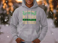 A person dons a Garment Graphics gray hoodie featuring the humorous English etiquette quote, If an Englishman gets run over by a truck he apologizes to the truck, against a snowy outdoor backdrop with blurred lights.