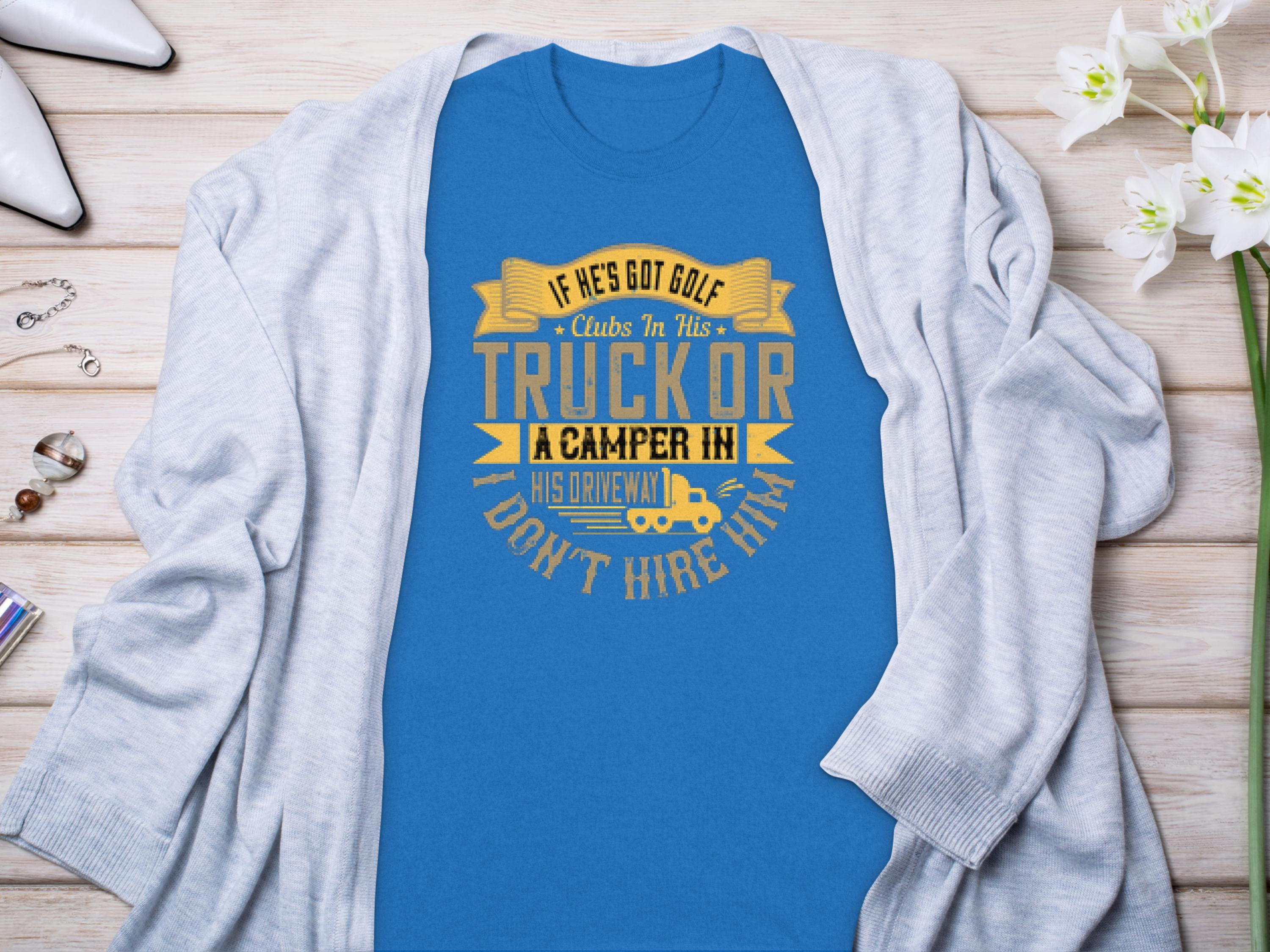 A Garment Graphics blue t-shirt with the funny graphic “If he’s got golf clubs in his truck or a camper in his driveway, don’t hire him,” styled on a gray cardigan surrounded by white flowers, jewelry, and shoes—ideal for those who appreciate camping humor.