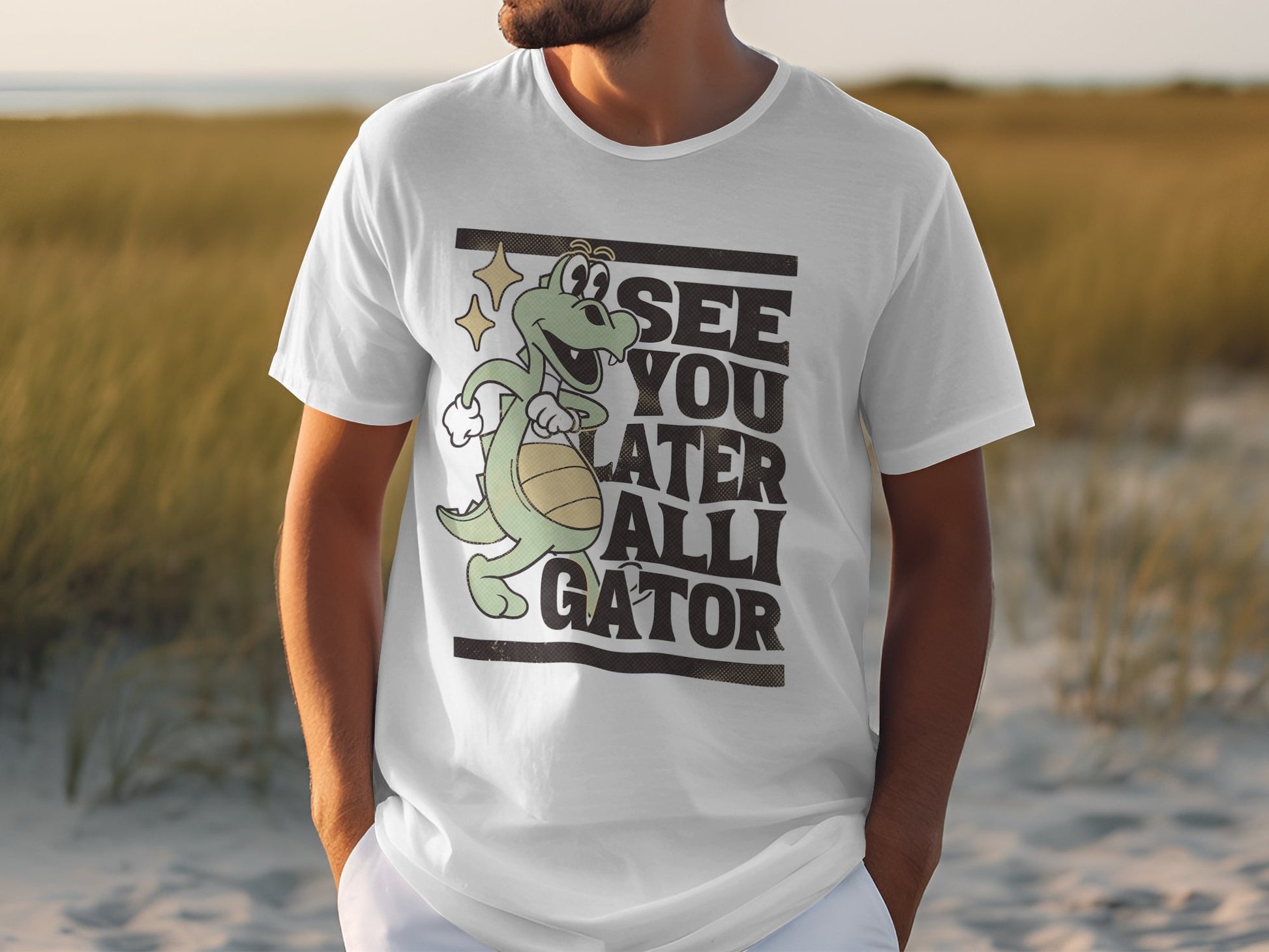A person sports a Garment Graphics casual T-shirt with a cartoon alligator holding a basketball and the humorous text See You Later Alligator. The background showcases a beach scene with sand and grass, capturing leisurely vibes.