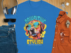 A Garment Graphics blue dog t-shirt features a pooch in sunglasses with Paw-sitive Stylish, Chillin Like A Canine Villain, styled with jeans, shades, headphones, a watch, and a brown shirt on a wooden surface.