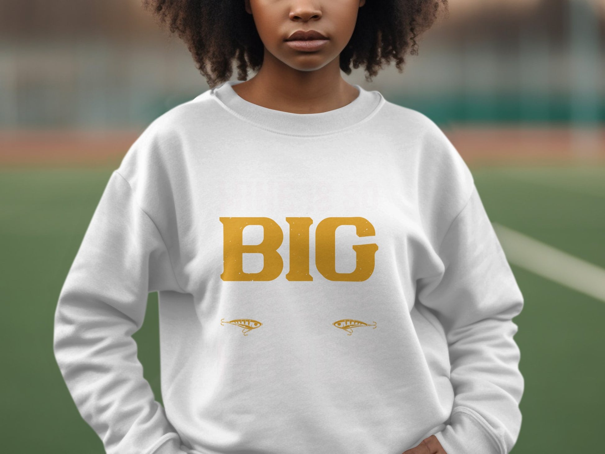 A person wears a distinctive Garment Graphics sweatshirt featuring BIG in bold yellow letters. Decorative elements enhance its style below the text. The blurred outdoor background, possibly a sports field, highlights this as a bold statement piece for any casual occasion.