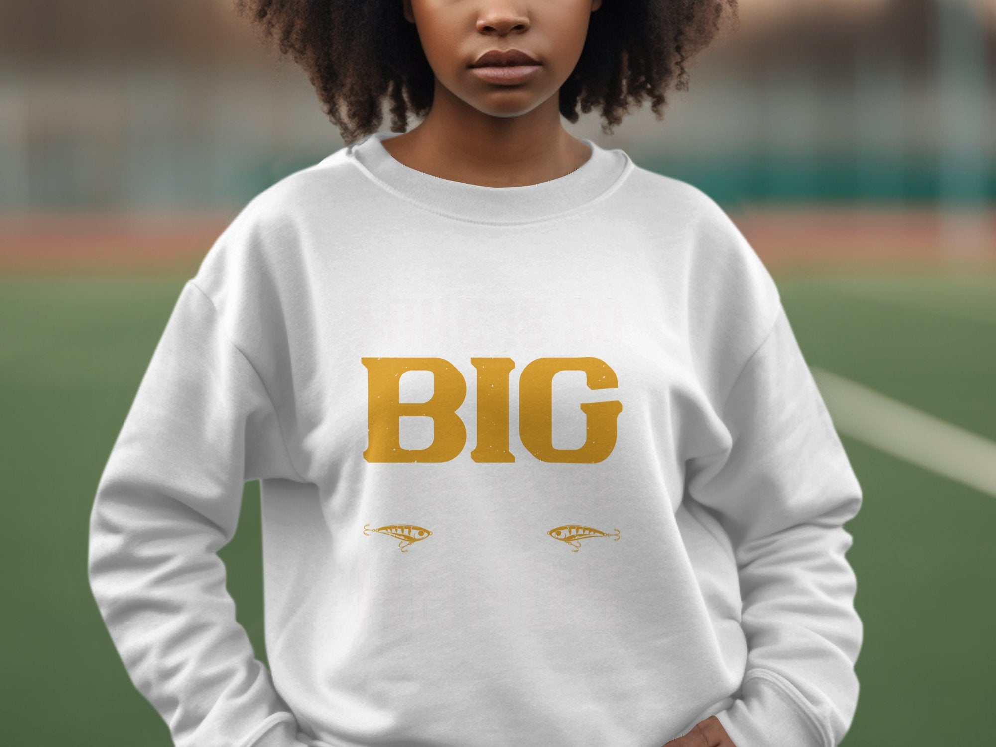 A person wears a distinctive Garment Graphics sweatshirt featuring BIG in bold yellow letters. Decorative elements enhance its style below the text. The blurred outdoor background, possibly a sports field, highlights this as a bold statement piece for any casual occasion.