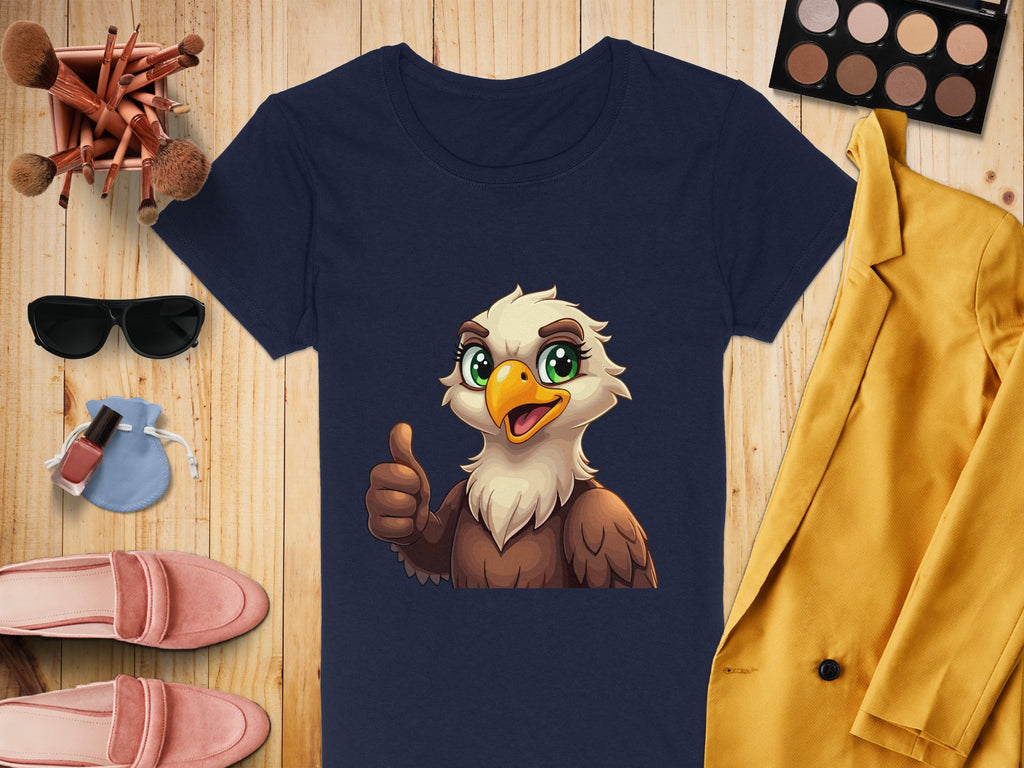 A Garment Graphics navy blue T-shirt with a cartoon eagle giving a thumbs-up is displayed on wood, surrounded by makeup brushes, a sunglasses case, yellow jacket, pink shoes, nail polish, and an eyeshadow palette—ideal for stylish animal lovers!.