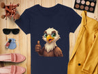 A Garment Graphics navy blue T-shirt with a cartoon eagle giving a thumbs-up is displayed on wood, surrounded by makeup brushes, a sunglasses case, yellow jacket, pink shoes, nail polish, and an eyeshadow palette—ideal for stylish animal lovers!.