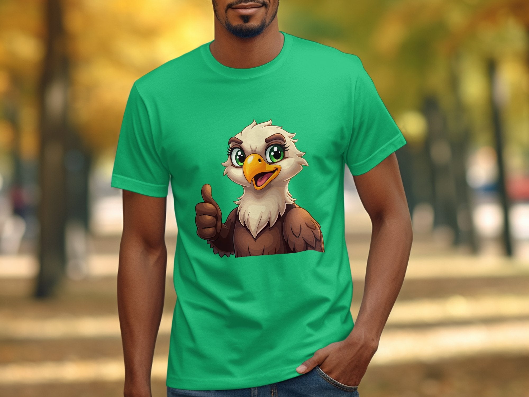 Wearing a green Garment Graphics T-shirt featuring a cartoon eagle giving a thumbs up, a man enjoys the outdoors with vibrant fall foliage in the background, adding fun to his casual wardrobe.