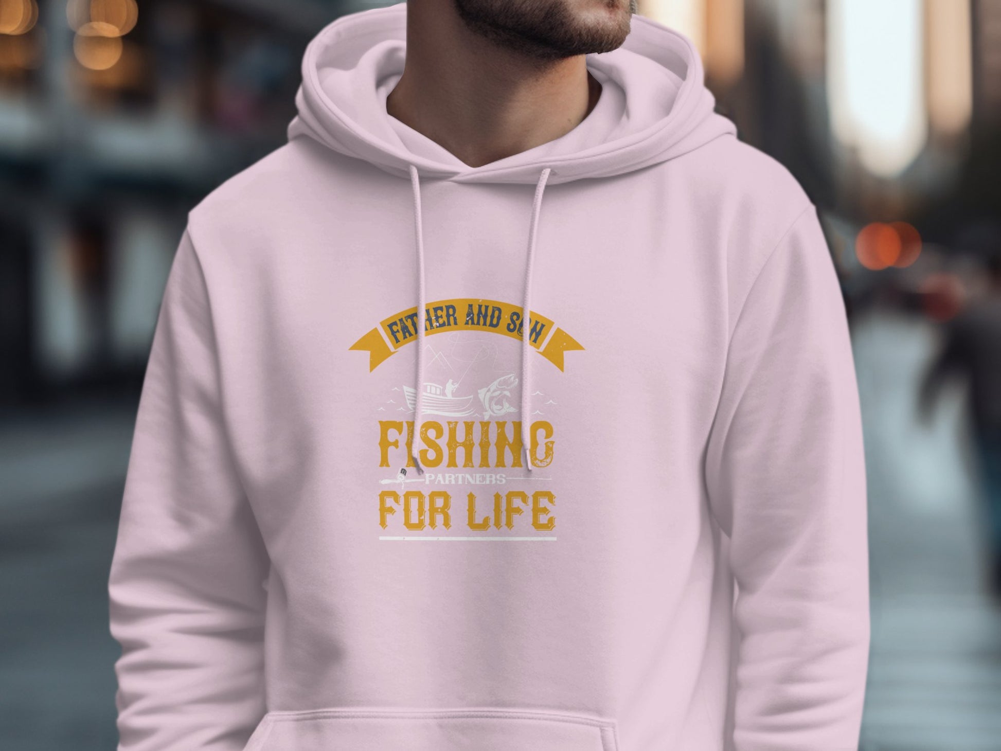 On a blurred city street, a person wears a Garment Graphics fishing hoodie. The white hoodie, ideal for fishing enthusiasts, features yellow text with a fish design that reads Father and Son Fishing Partners for Life.