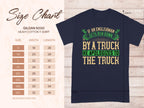 A navy blue T-shirt from Garment Graphics features a witty design with the text If an Englishman gets run down by a truck he apologizes to the truck in green, beige, and gold. Available in sizes S to 5XL with measurements shown on the left. Ideal for fans of humorous English politeness-themed tees.