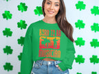 A woman joyfully poses before a wall of green shamrocks, wearing Garment Graphics unisex green sweater with Born to Be Musician emblazoned on it, celebrating her love for music. Her long hair frames her smiling face, showcasing her musical passion.