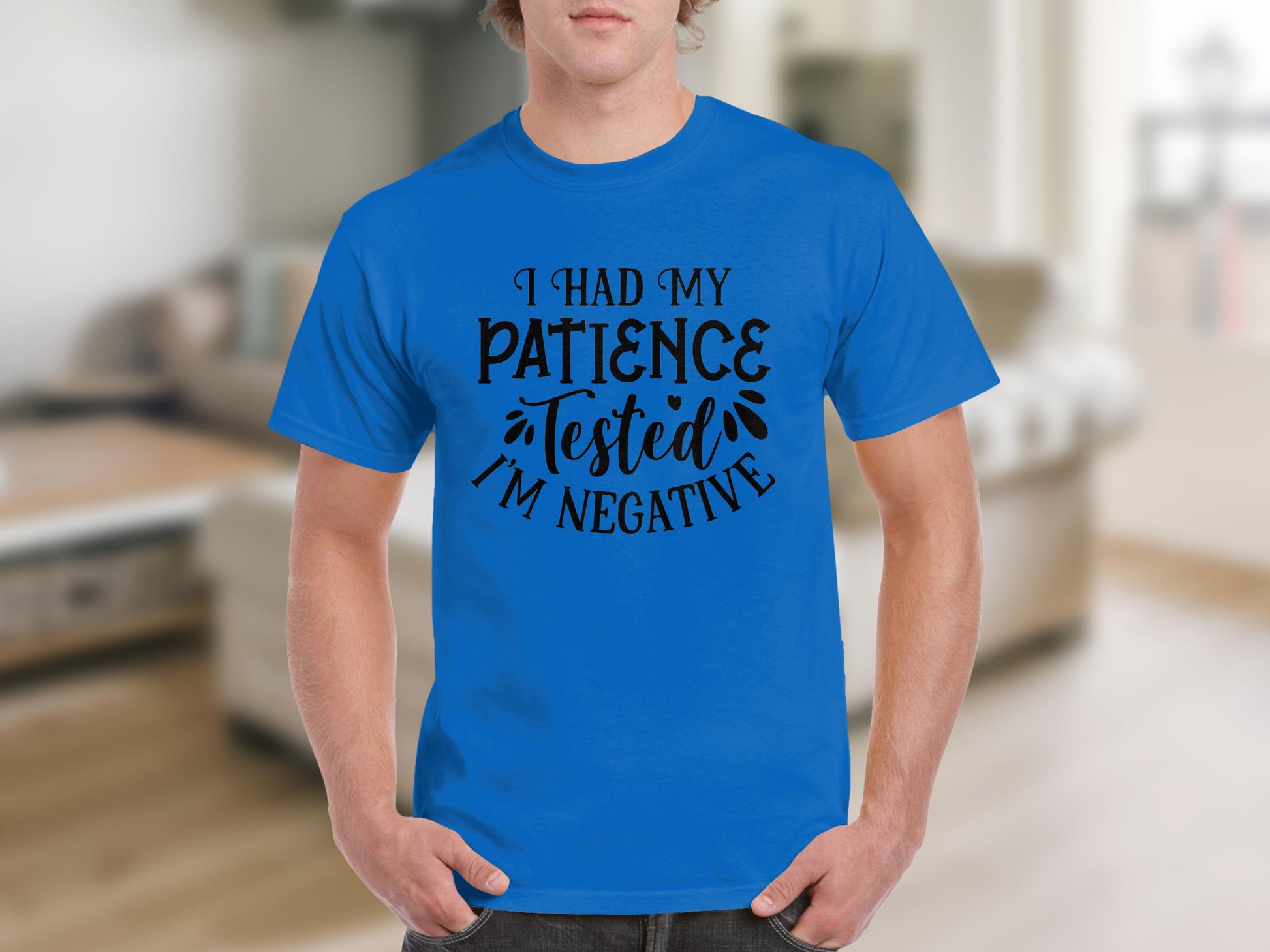 Someone is sporting a Garment Graphics T-shirt that humorously says, I Had My Patience Tested. Im Negative, reflecting sarcasm. The background reveals a blurred interior with a couch and rug.