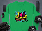 Garment Graphics urban-style green sweatshirt showcases a vibrant I Love Graffiti design with spray paint elements, styled on a flat neutral background amidst a smartphone, smartwatch, sneakers, wireless speaker, and dumbbells.