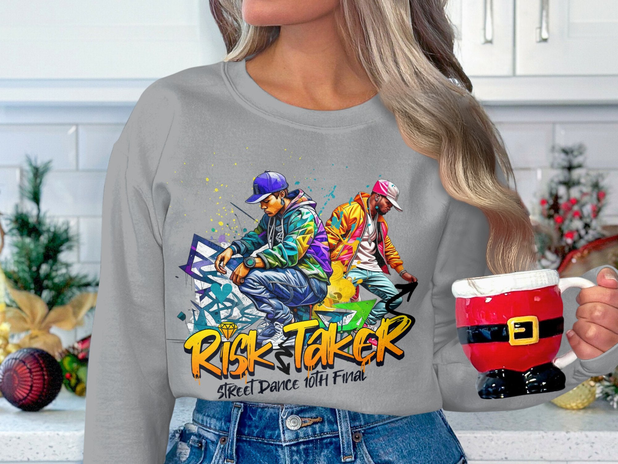 Sporting Garment Graphics gray sweatshirt featuring a lively design of two dancers and Risk Taker Street Dance 10th Final, they hold a Santa-style mug. Festive holiday decorations enhance the kitchen, embodying the street dance finals spirit.