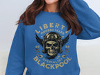 A woman wears a blue sweatshirt featuring a skull with goggles and wings, capturing the biker style. The text says Liberty Motorcycles Blackpool Specialist 2023. Brand: Garment Graphics.