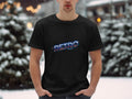 Adorned in a Garment Graphics black t-shirt featuring Retro in colorful, bold letters, an individual radiates vintage charm against a snowy setting with blurred trees and lights, capturing the classic allure of retro graphic design.