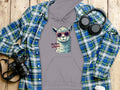 Garment Graphics classic fit gray hoodie features a llama in funny sunglasses with the text No Prob-llama. Styled with a blue plaid shirt, black headphones, a camera, and a white travel coffee cup on a wooden surface.