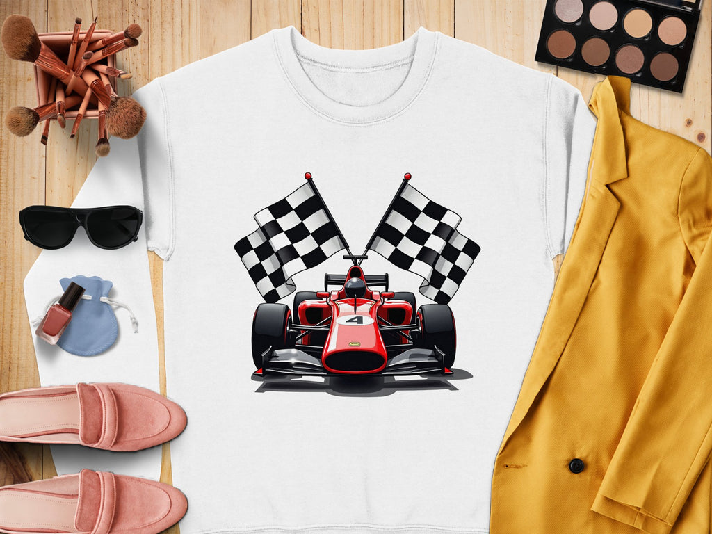A flat lay features a vibrant Garment Graphics sweatshirt with a racing car and checkered flags, perfect for motorsport fans. The scene includes makeup brushes, sunglasses, a makeup palette, lipstick, a ring pouch, pink loafers, and a mustard blazer.