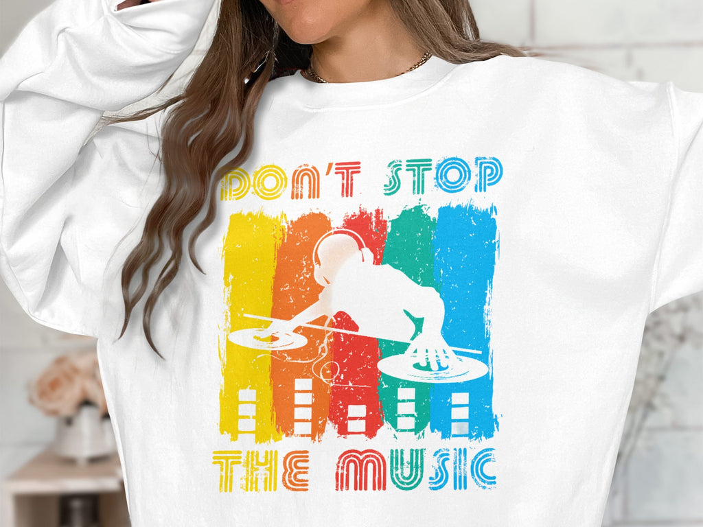 Sporting a Garment Graphics white sweatshirt featuring a vibrant DJ design, the text DONT STOP THE MUSIC stands out against vertical stripes in yellow, red, green, and blue. Perfect for music lovers, the wearers face is unseen.