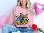 A person in a Garment Graphics pink sweatshirt with the print, Risk Taker Street Dance 10th Final, holds a red rose, smiling in ripped jeans amid pink heart-shaped balloons, celebrating the street dance finals.