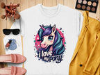 Flat lay of a Garment Graphics white graphic sweatshirt with a ponyunicorn design and I love my pony text, surrounded by sunglasses, makeup brushes, a palette, pink loafers, blue drawstring pouch, nail polish, and yellow jacket on wooden surface.