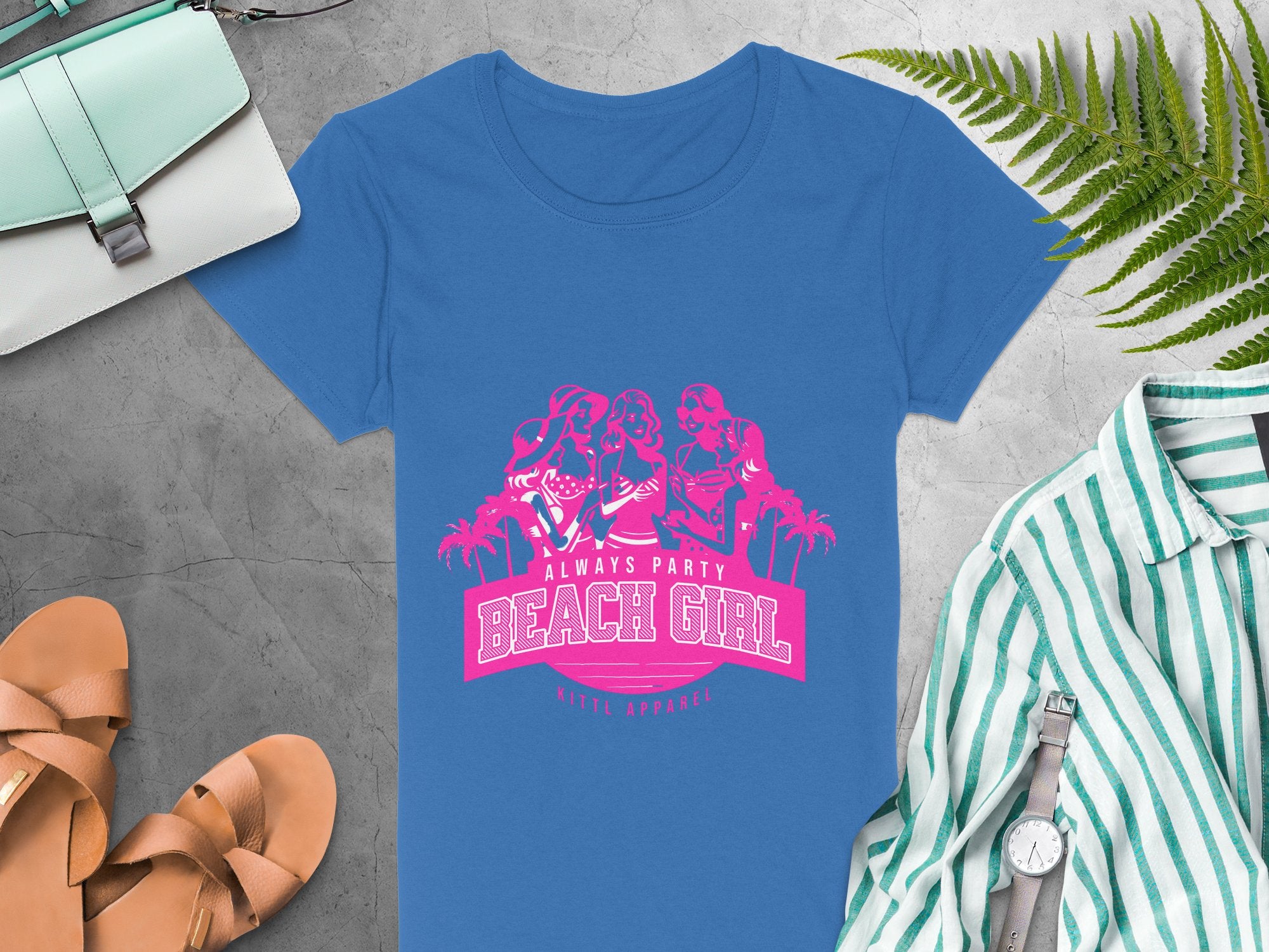 Blue t-shirt featuring a pink graphic of three dancing women with Always Party Beach Girl and Ninth Apparel, surrounded by a purse, sandals, striped shirt, watch, and fern leaves on gray. Ideal for Womens Semi-Fitted Tee lovers from Garment Graphics.