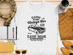 A flat lay showcases Garment Graphics white T-shirt, featuring a vintage car design and Classic London City Vintage Car Club, Classic Garage text. The scene includes a yellow purse, sunglasses, notebook, pen, plaid scarf, and steaming coffee.