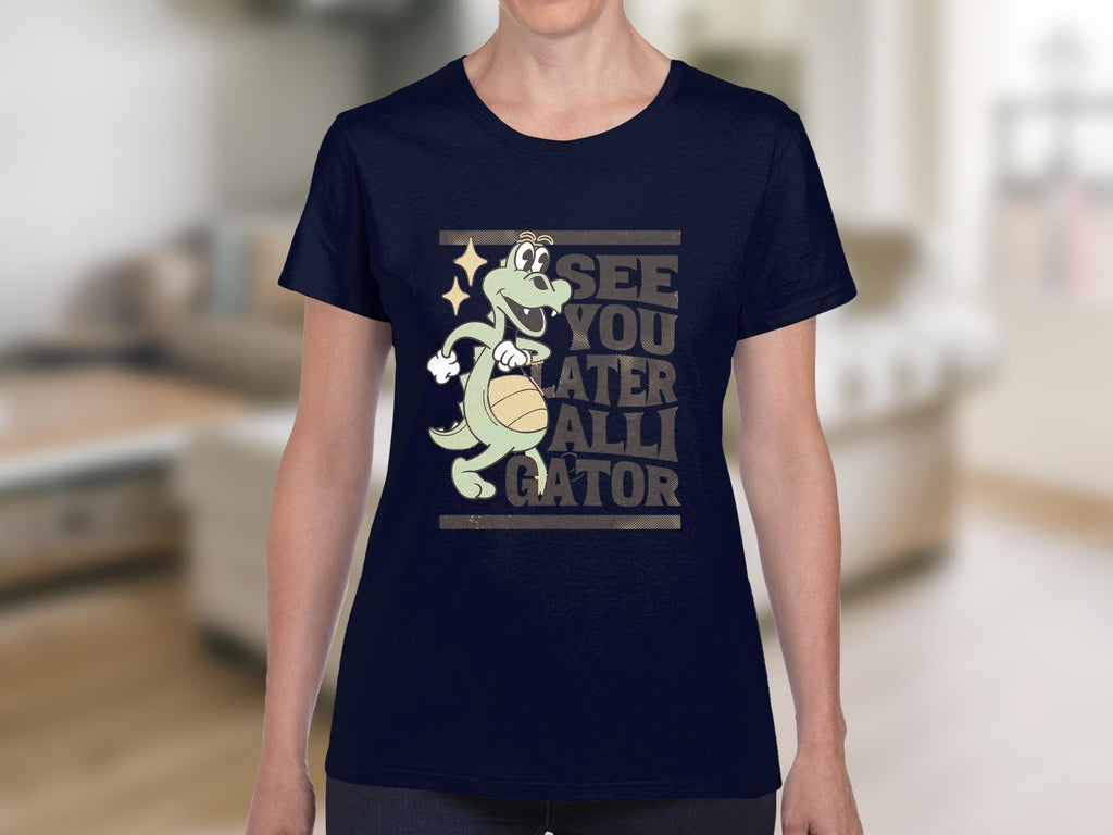 A person is wearing a Garment Graphics navy blue T-Shirt featuring a cartoon alligator holding a basketball and the funny text SEE YOU LATER ALLIGATOR, set against a blurred living room backdrop. The playful design is ideal for women.