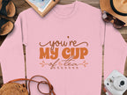 A cozy pink Garment Graphics sweatshirt with Youre My Cup of Tea in vibrant orange text, paired with sandals, a notebook, straw hat, sunglasses, and white instant camera on a wooden surface. Unisex sizing guarantees the ideal fit for everyone.