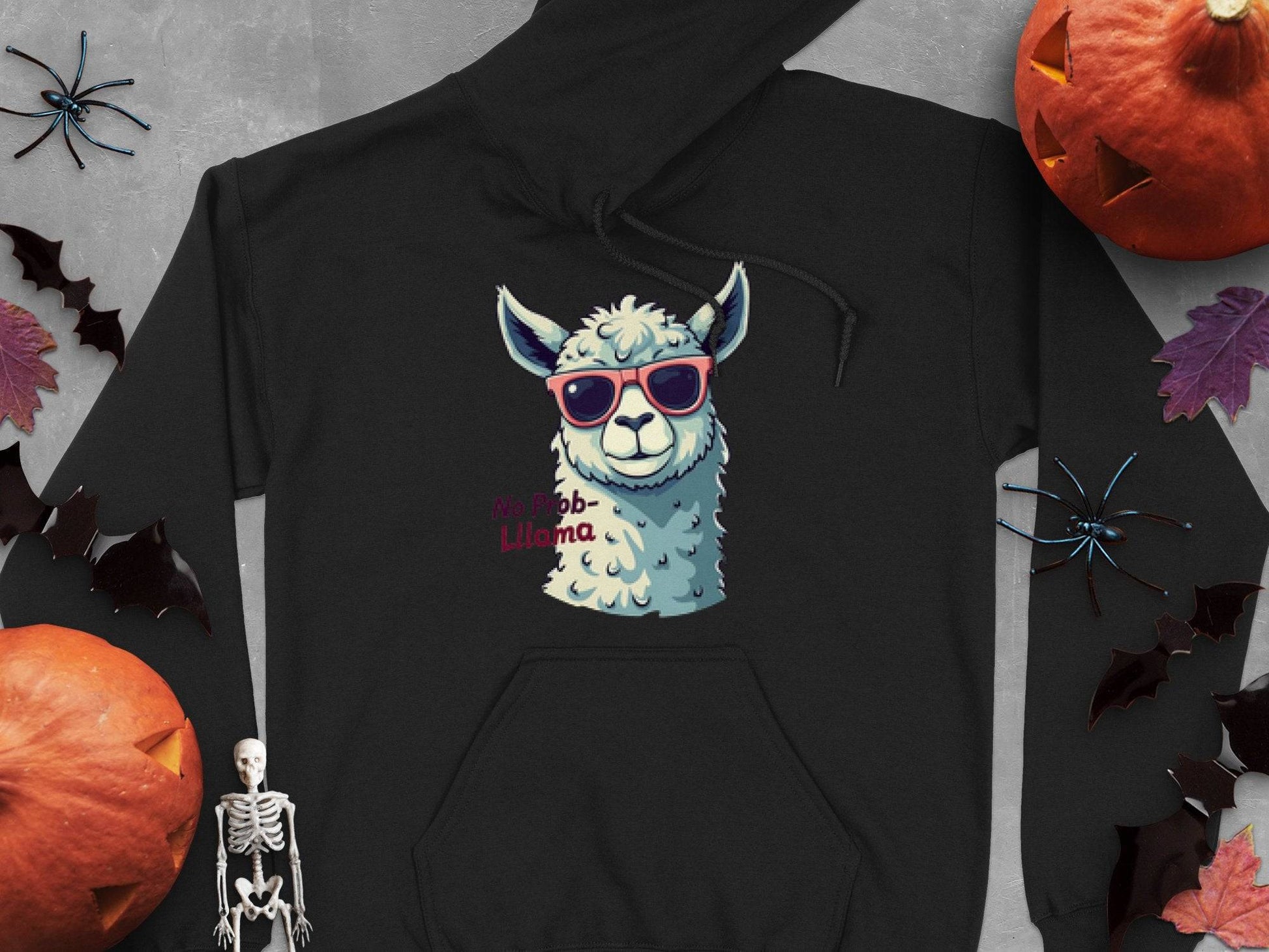 Garment Graphics classic fit black hoodie features a llama in red sunglasses, with the text No Prob-Llama, surrounded by Halloween elements like a skeleton, bats, and pumpkins on a gray background.