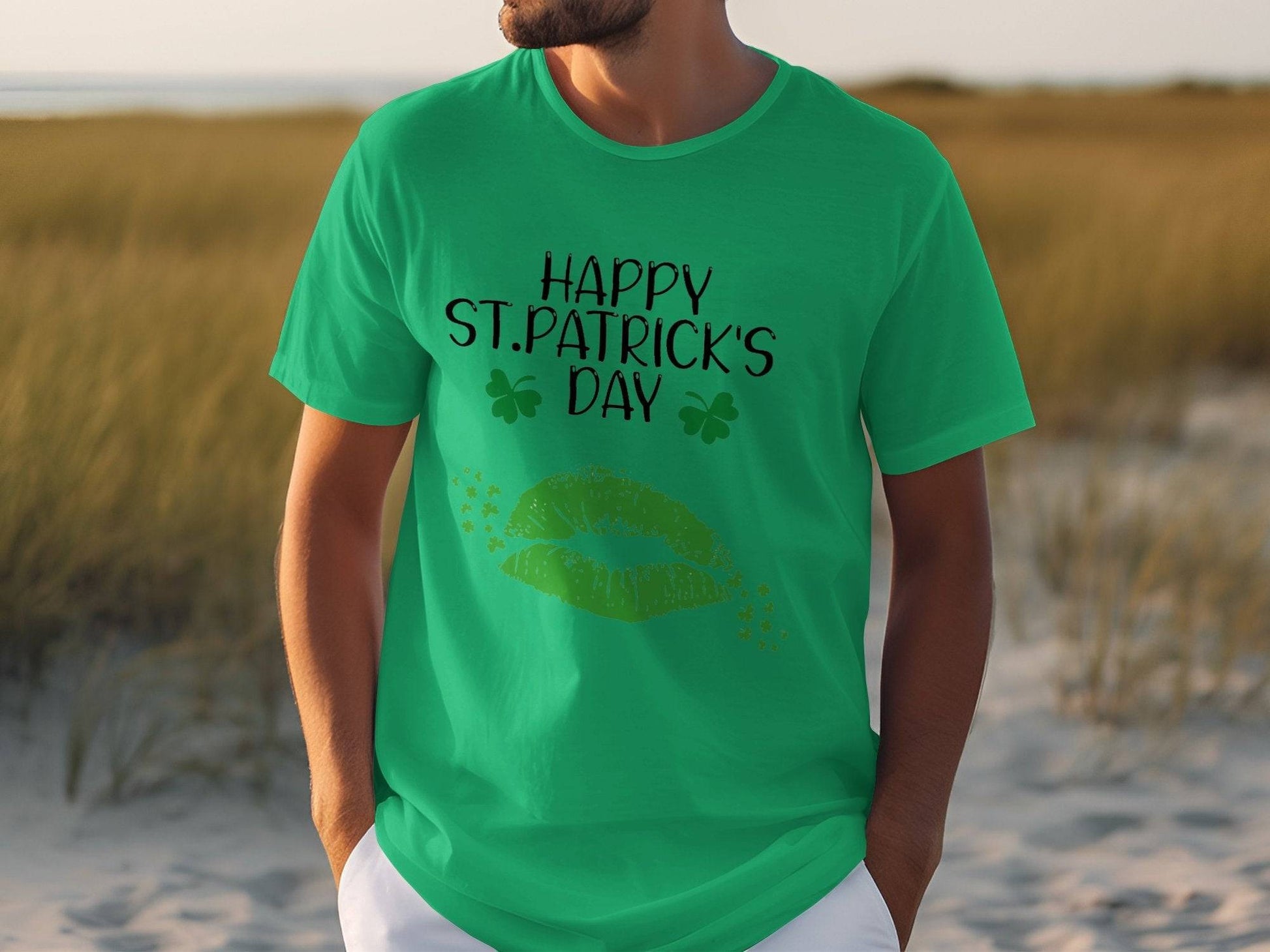 A person in a grassy area wears a Garment Graphics T-shirt featuring Happy St. Patricks Day with two shamrocks and vibrant green lips, capturing the festive spirit.
