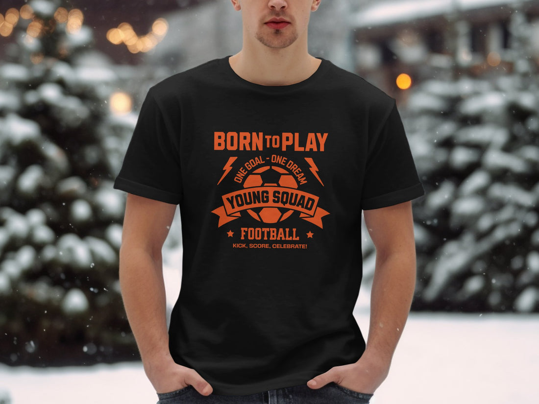 A person wears a Garment Graphics white T-shirt featuring bold orange text, Born to Play: One Goal One Dream, with Young Squad Football and a soccer ball graphic. It reads Kick. Score. Celebrate! over a vibrant grassy background.