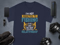 The Garment Graphics blue fishing T-shirt, ideal for anglers, showcases the text Im not addicted to fishing, we are just in a very committed relationship, alongside a smartphone, smartwatch, sneakers, dumbbell, and portable speaker on a gray surface.