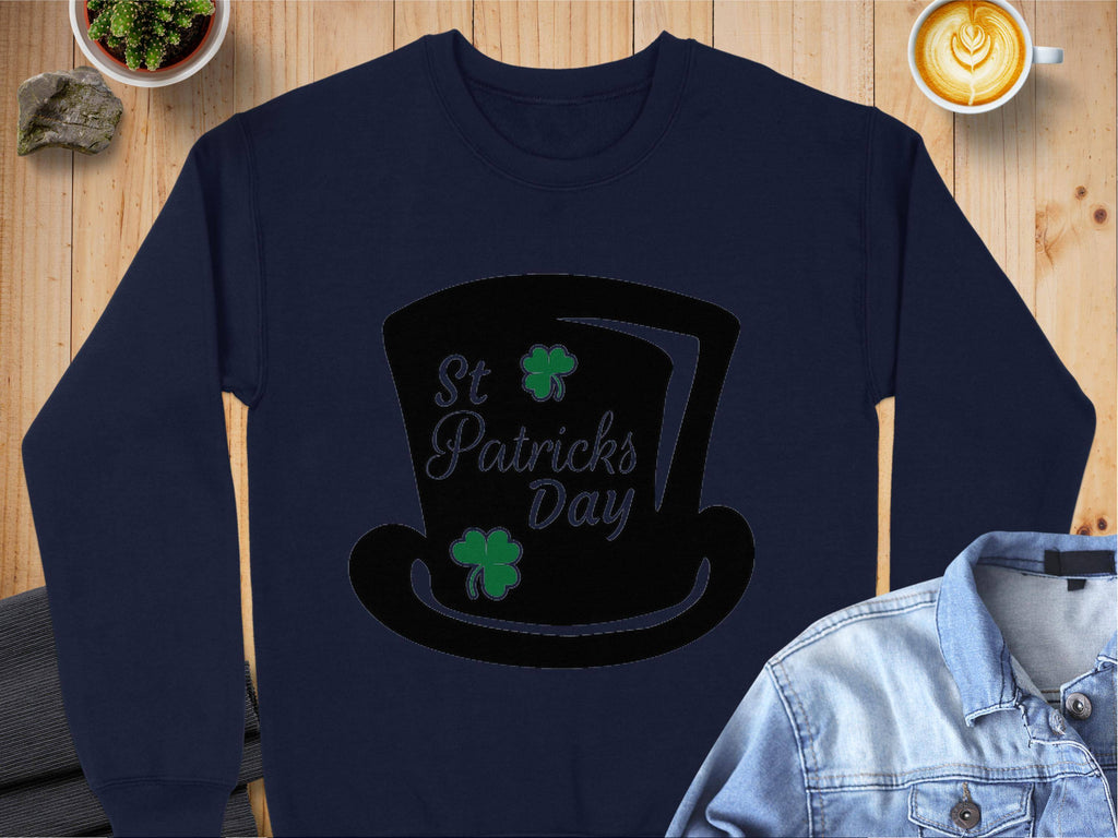 A Garment Graphics navy blue sweatshirt features a black top hat, St Patricks Day, and two green shamrocks. It exudes festive vibes on a wooden surface alongside a denim jacket, latte cup, and small plant.