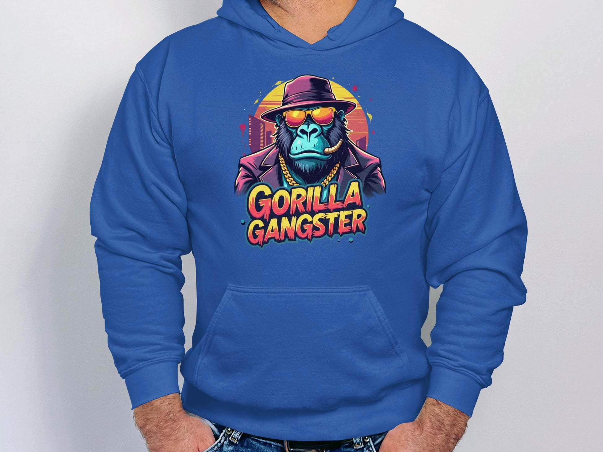 Sporting a blue hoodie from Garment Graphics, a man showcases striking gorilla artwork featuring a gorilla with a hat and sunglasses. The Gorilla Gangster text enhances its appeal, making it a standout in streetwear fashion.