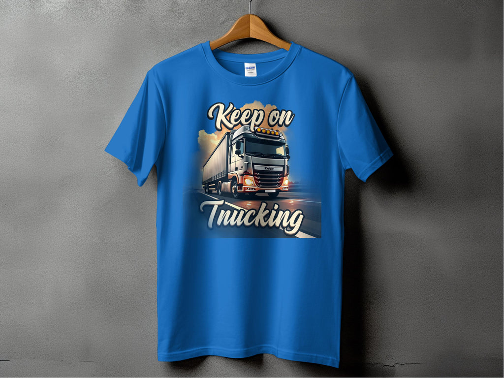A Garment Graphics blue T-shirt on a wooden hanger against a gray backdrop features a graphic of a large truck on the road with Keep on Trucking above and below, ideal for truck enthusiasts.