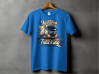 A Garment Graphics blue T-shirt on a wooden hanger against a gray backdrop features a graphic of a large truck on the road with Keep on Trucking above and below, ideal for truck enthusiasts.
