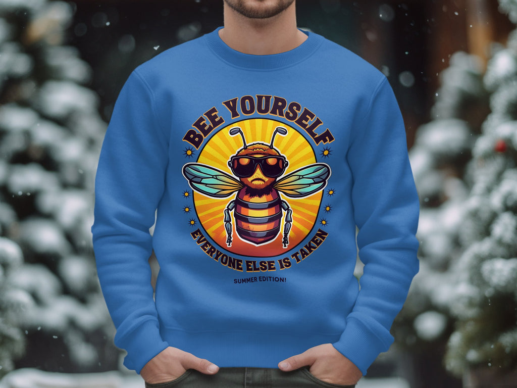A person wears Garment Graphics blue Summer Edition Sweatshirt featuring a cool bee in sunglasses. The phrase Bee Yourself, Everyone Else is Taken pops against the snowy backdrop, highlighting its unisex sizing allure.