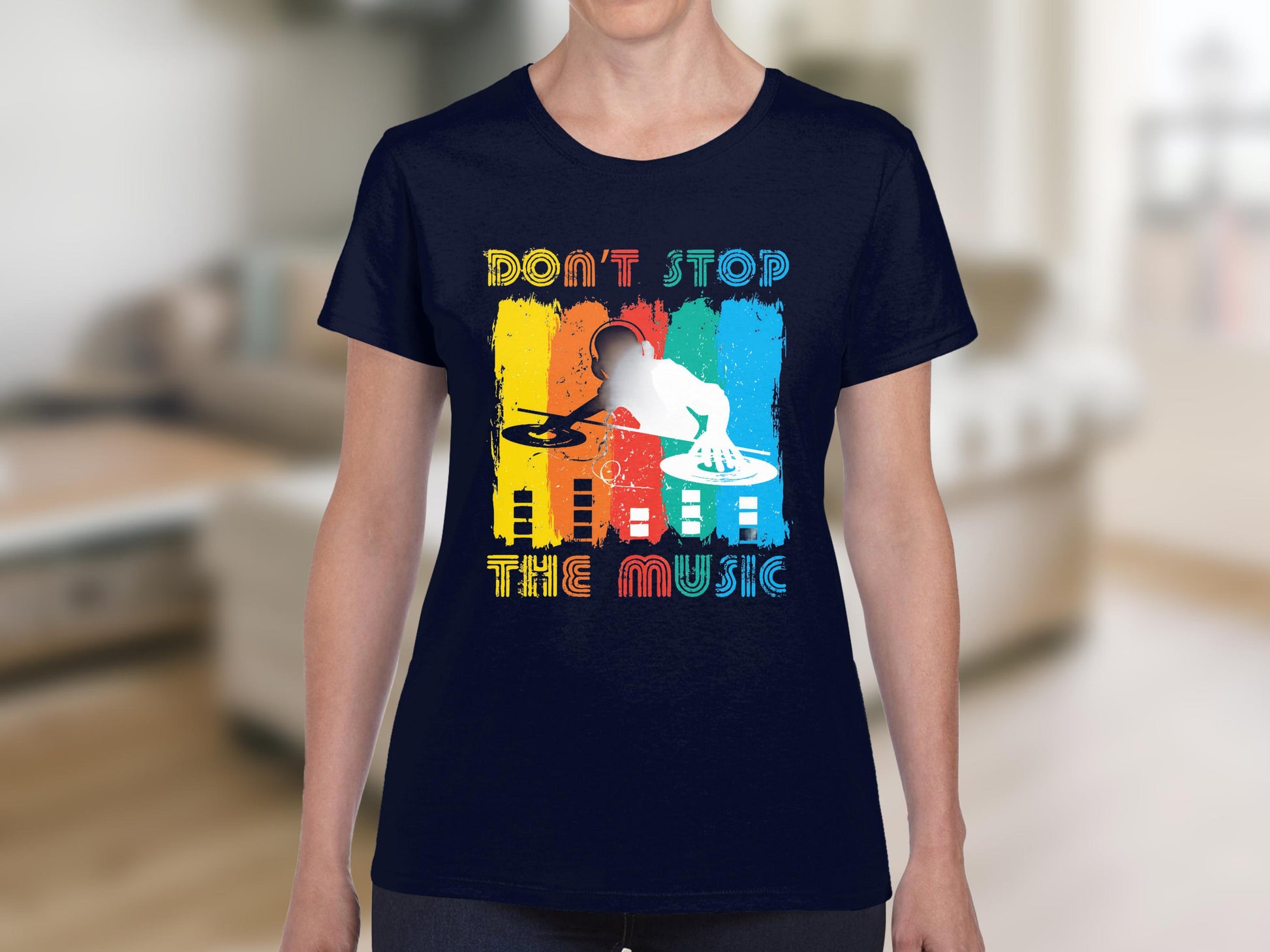 Someone is wearing a vibrant navy blue DJ graphic tee from Garment Graphics, featuring a DJ at the turntable with colorful vertical stripes and the slogan Dont Stop the Music in bold, set against a blurred indoor background.