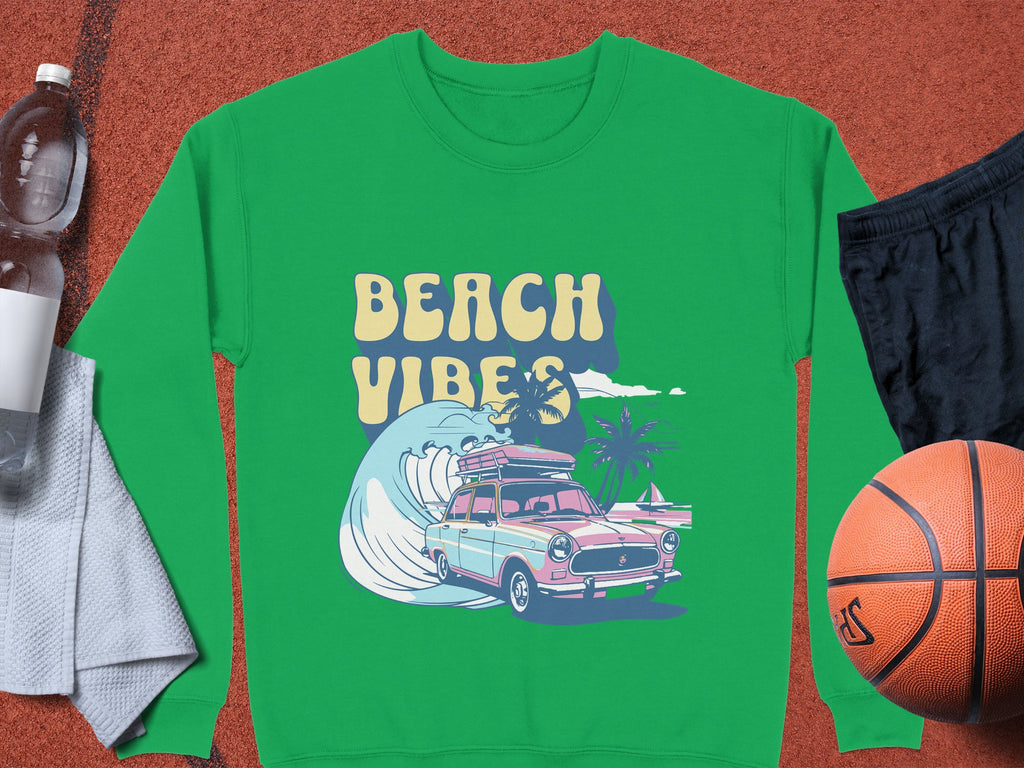 A green Beach Vibes graphic sweatshirt by Garment Graphics features a vintage car with surfboards, waves, and palm trees. In unisex sizing, it complements a water bottle, towel, black shorts, and basketball for retro road trip vibes.