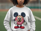 Someone is wearing a white sweatshirt from Garment Graphics featuring a donut character with large ears, gloves, red shoes, and a sprinkle-textured body. The fun design comes in unisex sizing and is displayed against a blurred outdoor scene.